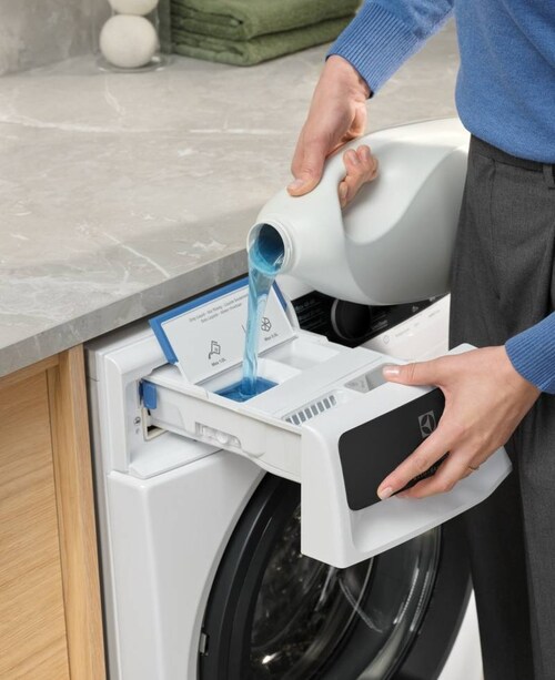 Person pouring detergent into Electrolux washing machine.