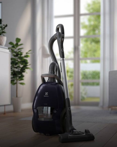 A bagged vacuum cleaner is standing in front of a window.